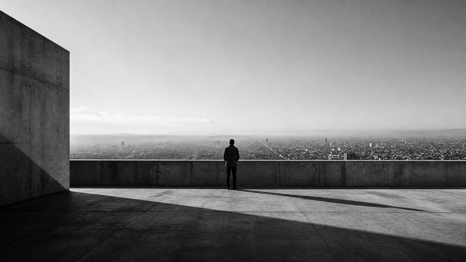 A lone figure on a high concrete overlook above the city